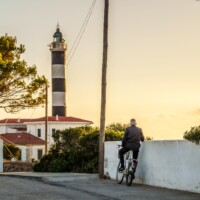 Alter Mann steht mit Fahrrad vor Leuchtturm auf Mallorca Alter Mann steht mit Fahrrad vor Leuchtturm auf Mallorca